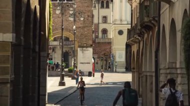 Treviso, İtalya 1 Ocak 2025: İnsanlar Treviso, İtalya 'da tarihi bir ara sokakta bisiklet sürüyor ve yürüyor. İçinde kemerli mimari ve kaldırım taşı sokaklar var.
