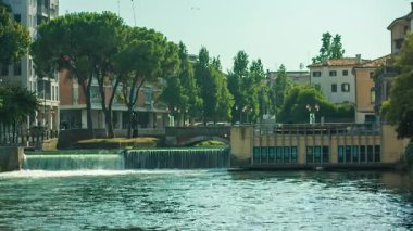 Treviso, İtalya 1 Ocak 2025: Treviso, İtalya 'da bir köprünün altından akan sular, arka planda binalar ve ağaçlarla birlikte