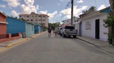 Bayahibe, Dominik Cumhuriyeti 1 Ocak 2025: Dominik Cumhuriyeti 'nin Bayahibe kentinde renkli binalar ve park edilmiş arabalarla dolu asfalt bir sokakta yürüyen turistler