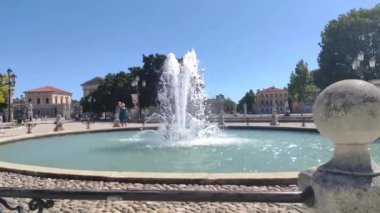 Padova, İtalya 1 Ocak 2025: Padua, İtalya 'da açık mavi gökyüzünün altında, arkasında ağaçlar ve klasik binalar bulunan tarihi bir meydanda su sıçrayan fıskiye