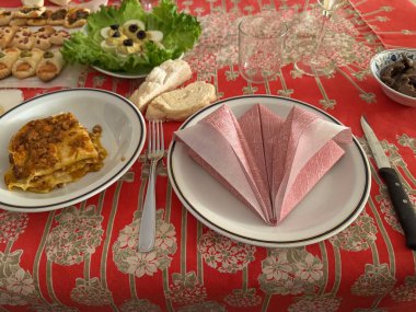 Öğle yemeği için masada sunulan lazanya aperatifler, ekmek, katlanmış peçeteler, boş bardaklar ve çatal bıçaklar sıcak ve davetkar bir atmosfer yaratıyor.