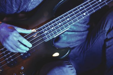 Canlı bir müzik performansının enerjisini ve tutkusunu canlı bir atmosferde yakalayan canlı mavi sahne ışıkları altında ustalıkla bas gitar çalan ellerin yakın görüntüsü
