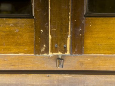 Close-up of an old, weathered wooden door, highlighting the worn varnish, exposed wood grain, and a metal latch holding the door firmly closed, suggesting age, history, and the passage of time clipart