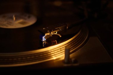Turntable iğnesi sıcak ışıkta vinil plak çalıyor, nostalji ve müzik zevkini çağrıştırıyor
