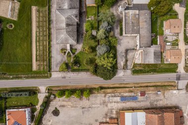 Hava perspektifi, yerleşim alanlarını ve ekili alanları ayıran ve kırsal ve kentsel unsurların bir karışımını gösteren sakin bir kırsal yol yakalıyor.