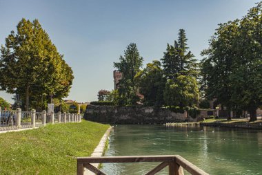 Treviso, İtalya 1 Ocak 2025: Treviso, İtalya 'da bereketli ağaçlar, antik duvarlar ve ortaçağ kulesiyle sakin bir şehir manzarası yaratan Cagnan Büyük Kanalı manzarası