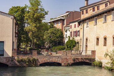 Treviso, Italy 1 January 2025: Cagnan grando canal flowing under a small brick bridge with typical italian houses in the background in treviso, italy clipart