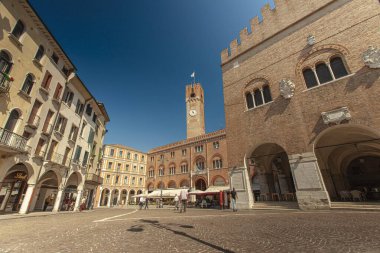 Treviso, İtalya 1 Ocak 2025: Güneşli bir yaz gününde İtalya 'nın Treviso kentinde bulunan Palazzo dei trecento ve sivil kulesiyle Piazza dei signori' de yürüyen turistler