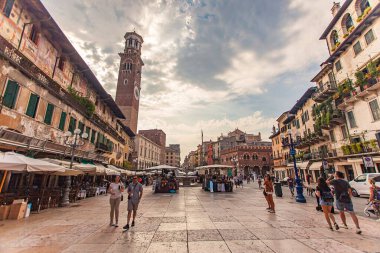 Verona, İtalya 1 Ocak 2025: İtalya 'nın Verona kentinde pazar tezgahları ve Torre dei Lamberti ile birlikte yürüyen turistler, Verona, İtalya' da bulutlu bir yaz gününde