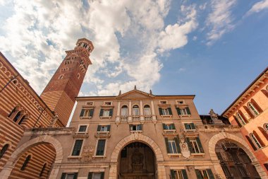 Verona, Italy 1 January 2025: Low angle view of historical buildings and the lamberti tower under a cloudy blue sky in piazza delle erbe, verona, italy clipart