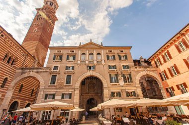 Verona, İtalya 1 Ocak 2025: İtalya 'da arka planda Torre dei lamberti ve Palazzo della ragione ile Piazza delle erbe' yi işgal eden açık hava kafeleri