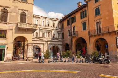 Verona, İtalya 1 Ocak 2025: Piazza delle erbe 'ye park etmiş elektrikli scooterlar turistler ve yerel halkla birlikte İtalya' nın Verona kentinde yürüyor