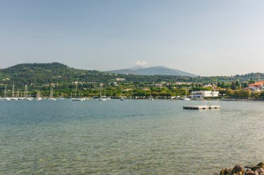 Garda Gölü, İtalya 3 Ocak 2025: Bardolino yakınlarındaki Garda Gölü 'ne demirlemiş yelkenliler ve güneşli bir günde Monte Baldo görülebilir.