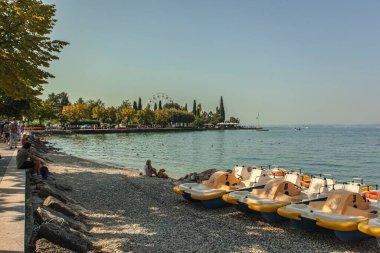 Garda Lake, Italy 3 January 2025: Pedal boats on the shore of lake garda, with tourists enjoying the sunny day clipart