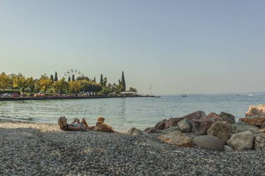 Garda Lake, Italy 3 January 2025: Tourist enjoying summer holidays with her dog on the pebble beach of bardolino, lake garda, italy clipart