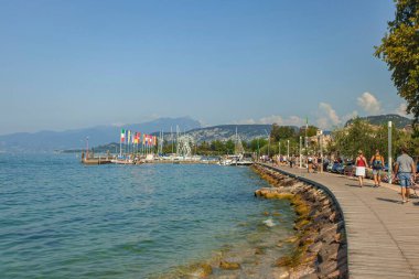 Garda Gölü, İtalya 3 Ocak 2025: Bardolino 'daki sahil yolunda yürüyen turistler, İtalya' nın Garda Gölü 'nde güzel bir yaz gününün tadını çıkarıyorlar.
