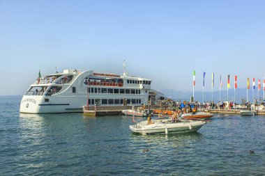 Garda Gölü, İtalya 3 Ocak 2025: Turistler yaz tatilinde İtalya 'nın Garda Gölü' nde tekne gezisinin keyfini çıkarırken, arka planda uluslararası bayraklar sallanıyor