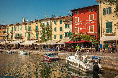 Garda Gölü, İtalya 3 Ocak 2025: İnsanlar kıyı boyunca demirlemiş renkli binalar, restoranlar ve teknelerle Garda Gölü 'nde yaz tatillerinin keyfini çıkarıyorlar