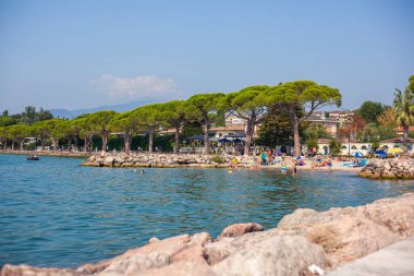 Garda Gölü, İtalya 3 Ocak 2025: Bereketli çam ağaçlarıyla çevrili İtalya 'nın Garda kentinde Bardolino' da yüzen ve güneşlenen turistler