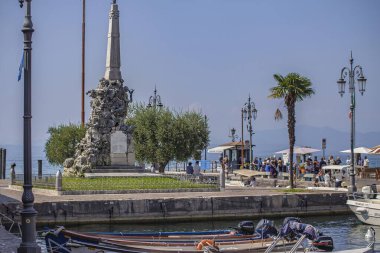Garda Gölü, İtalya 3 Ocak 2025: Turistler Bardolino, İtalya 'daki anıtın yakınındaki Garda Gölü kıyılarında güneşli bir günün tadını çıkarıyorlar