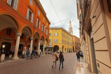 Modena, İtalya 1 Ocak 2025: Modena, İtalya 'da renkli binalar ve arka planda ghirlandina kulesiyle bir sokakta yürüyen iki turist