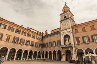 Modena, İtalya 1 Ocak 2025: Modena, İtalya 'da gökyüzü bulutlu, gökyüzü altında büyük meydanı gören kemerli ve pencereli Palazzo saat kulesi