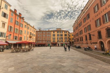 Modena, İtalya 1 Ocak 2025: Modena, İtalya 'da meydanda yürüyen insanlar, caddenin kenarına renkli binalar, kafeler ve motosikletler park etmiş durumda.