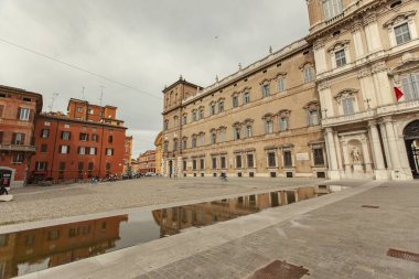 Modena, Italy 1 January 2025: Ducal palace is reflecting in a puddle in piazza roma, modena, on a cloudy day clipart