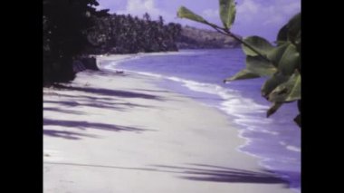 Denpasar, Bali Haziran 1985: 1985 'te çekilen bu klasik görüntüde tropikal bitki örtüsü bir Bali plajı ve uzak bir adanın manzarasını çerçeveler.