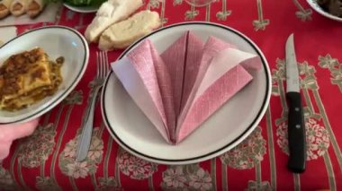 Kırmızı masa örtülü şenlik masası kademeli olarak lazanya, aperatifler ve gurme yemekleri ile doluyor. Kutlama için zarif bir hazırlık sergiliyorlar.