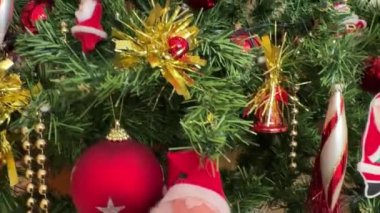 Noel Baba figürleri, kırmızı ve altın mücevherler, süslemeler ve diğer Noel süslemeleri ile süslenmiş Noel ağacı sıcak ve neşeli bir ortam yaratıyor.