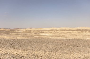 Göz alabildiğine kayalık bir arazi, arka planda dağlarla birlikte Mısır 'ın doğu çölünde berrak bir gökyüzünün altında uzanır.