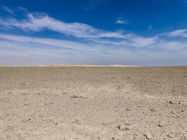 Parlak mavi bir gökyüzünün altında uzanan kayalık çöl manzarası Marsa alam, Mısır 'da dağınık bulutlar kurak arazi ve engin bir boşluk sergiliyor.