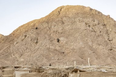 Bedeviler Mısır 'ın Marsa alam çölünde dik, kayalık bir dağa tırmanırken, ön planda geleneksel kulübeler görülebilir.