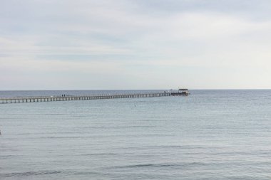 Mısırlı Marsa Alam 'ın sakin okyanus sularına uzanan uzun ve ahşap bir iskelenin sakin manzarası bulutlu bir gökyüzünün altında.