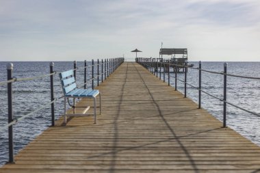 Marsa alam, Mısır 'da küçük bir kulübeye uzanan mavi banklı uzun ahşap bir iskele. Kızıl Deniz manzarası sunuyor.