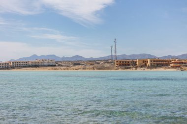 Sakin turkuaz sular, açık mavi gökyüzünün altındaki kıyı şeridini beneklendiren otellerle birlikte Mısırdaki Marsa Alam 'ın kumlu kıyılarına nazikçe yaklaşır.