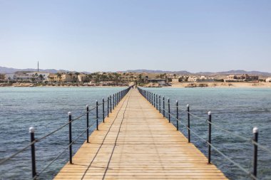 Sakin turkuaz sulara uzanan ahşap iskele, Marsa Alam, Mısır 'da sakin bir sahil manzarası sunan bir tatil köyüne doğru gidiyor.