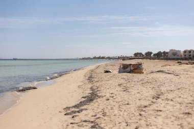 Terk edilmiş kiosk, kumlu bir plajda çürüyor, arka planda bir rıhtım ve tatil yeri var, Marsa Alam, Mısır 'da.