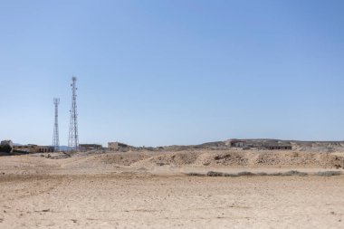 İki telekomünikasyon kulesi, Marsa alam, Mısır 'ın kurak çöl manzarasında açık mavi gökyüzüne karşı yükseliyor. Teknoloji ve doğa birleşiyor.