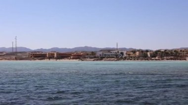 Sakin turkuaz su, arka planda oteller ve çöl dağları olan Marsa Alam, Mısır 'ın kumlu sahillerini nazikçe turlar.