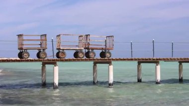 Marsa alam, Mısır 'ın turkuaz suları üzerinde ahşap iskele boyunca giden bagajlar güneşli bir günde huzurlu kızıl deniz kıyısı manzarasını gözler önüne seriyor.