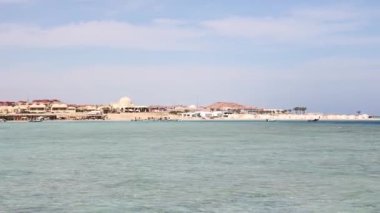 Sakin turkuaz su, uzaktan görülebilen binalar ve palmiye ağaçları ile Marsa alam, Mısır kıyılarını nazikçe turlar.