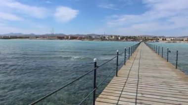 Ahşap iskele, Marsa Alam, Mısır 'da kristal berrak turkuaz suyu ve güneşli gökyüzü olan bir tatil köyüne doğru uzanır.