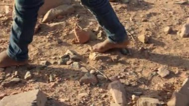 Çıplak ayaklı genç, kavurucu çöl arazisinden geçiyor, Marsa Alam 'ın sert Mısır ortamında kayalık kum arazisinde geziniyor, dayanıklı çocukluk yolculuğunu somutlaştırıyor.