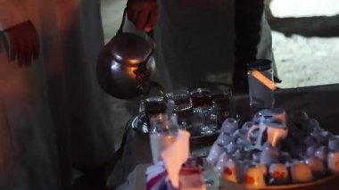 Bedevi adam sıcak çayı metal bir çaydanlıktan küçük bardaklara dolduruyor gece Marsa Alam çölünde, Mısır 'da bir tepside.