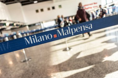 Milan, İtalya 13 Şubat 2025: Milan Malpensa havaalanı logosu ile kuyruk ayırıcıları ve arka planda yürüyen bulanık yolcular