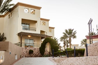 Marsa alam, Mısır 9 Şubat 2025: Balkonlu ve Mısır 'da palmiye ağaçlı otel odalarına giden kaldırım taşı yolu lüks ve tropik bir tatil deneyimi sunuyor.