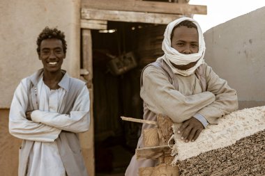 Marsa alam, 9 Şubat 2025: Geleneksel giyimli iki adam, Marsa alam çölündeki bir kır evinin dışında yerel kültür ve yoldaşlık sergiliyor.