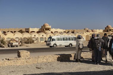 Marsa alam, Mısır 9 Şubat 2025: Marsa alam 'daki geleneksel Mısır mimarisine hayran olan bir grup turist, açık mavi gökyüzünün altında bir otobüs ve antika bir araba ile